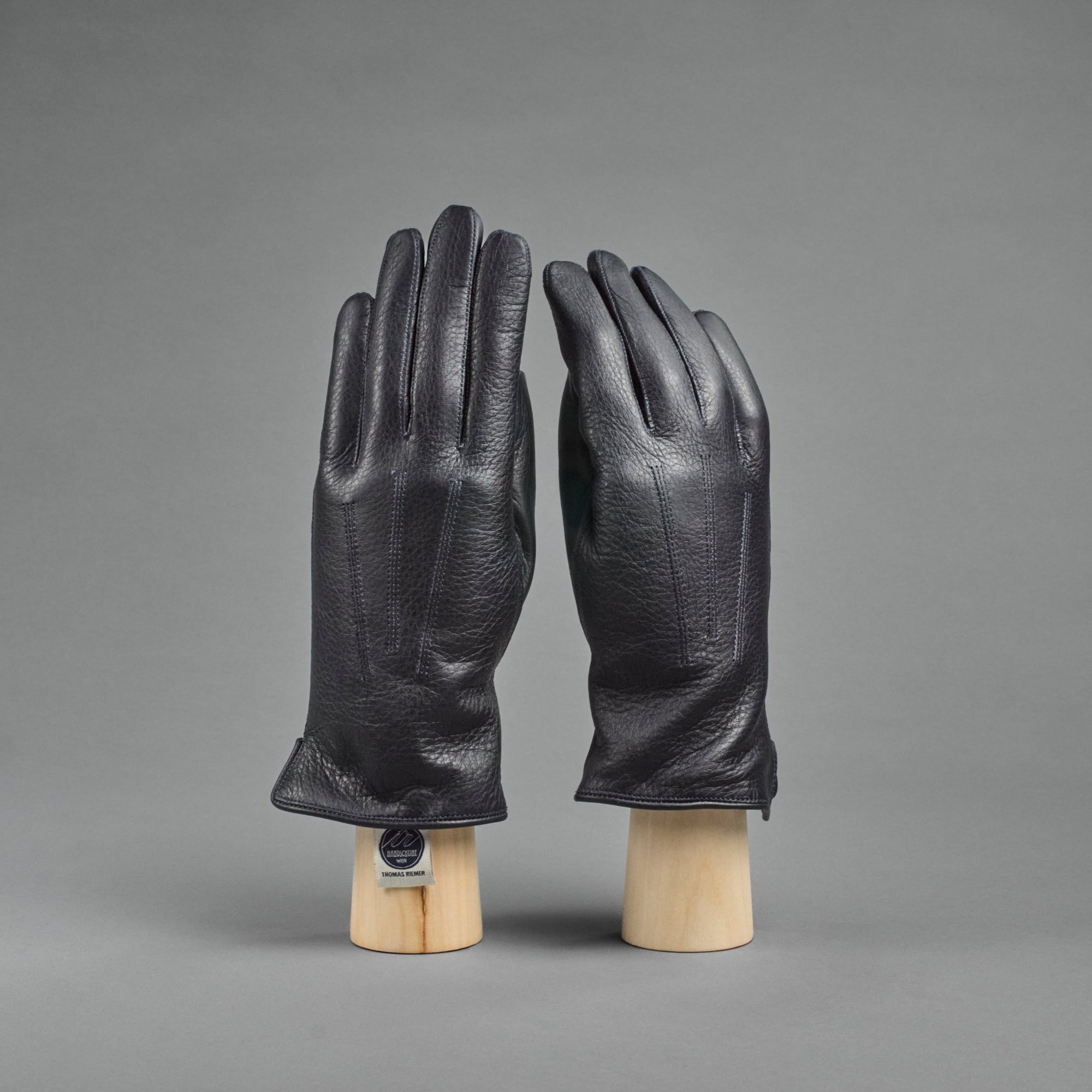 A pair of dark blue deerskin gloves lined with cashmere, displayed on a wooden stand against a grey background.